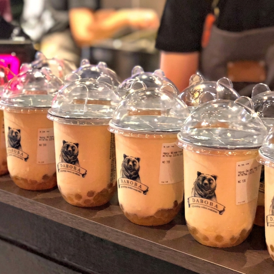 Rows of DABOBA bubble tea cups with tapioca pearls and dome lids displayed on a café counter, with staff in the background.