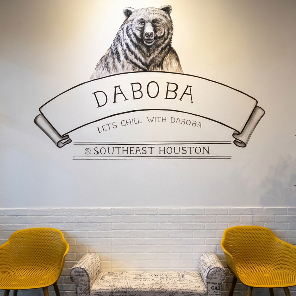 Daboba Southeast Houston lobby featuring a bear mural, yellow chairs, patterned sofa, and flowering tree.